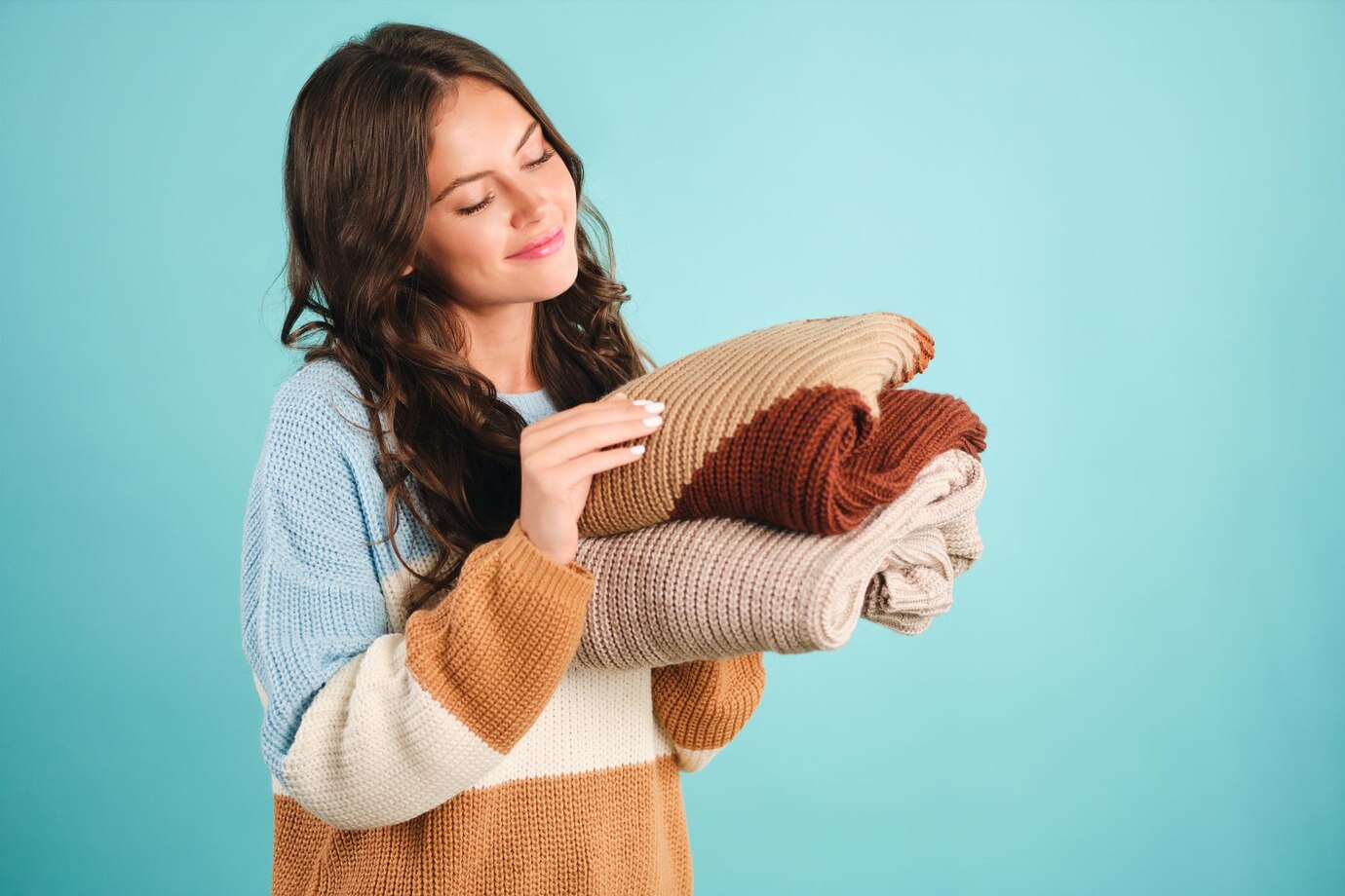 Beautiful cute girl dreamily holding cozy knitted sweaters in hands over blue background
