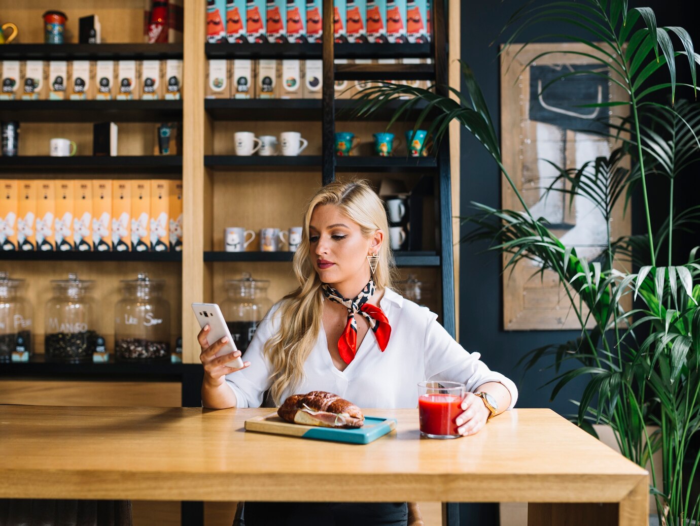 Pretty young woman using mobile phone holding glass of juice in caf